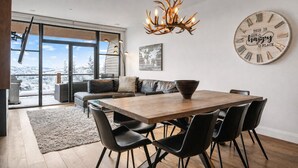 Un espace repas moderne avec une table en bois, des chaises noires et une grande horloge murale.