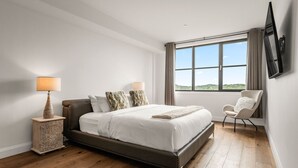 Une chambre à coucher moderne avec un grand lit, une table de chevet, une chaise et une fenêtre donnant sur un beau paysage.
