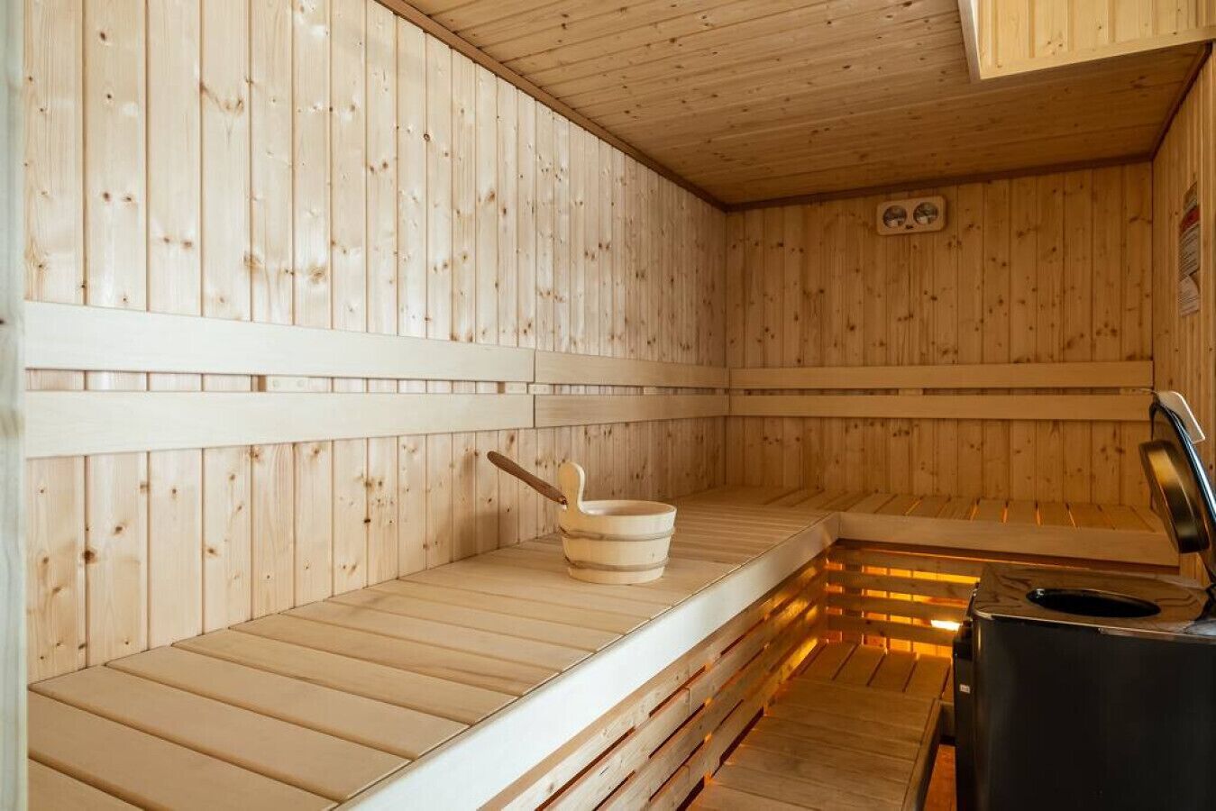 A sauna with wooden walls and benches, a wooden basin, and a heater.