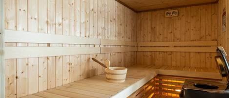 A sauna with wooden walls and benches, a wooden basin, and a heater.