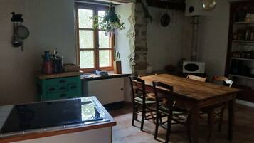 Een keuken met een houten tafel en stoelen, een raam met een plant, en een magnetron.