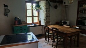 Una cocina con una mesa y sillas de madera, una ventana con una planta y un microondas.