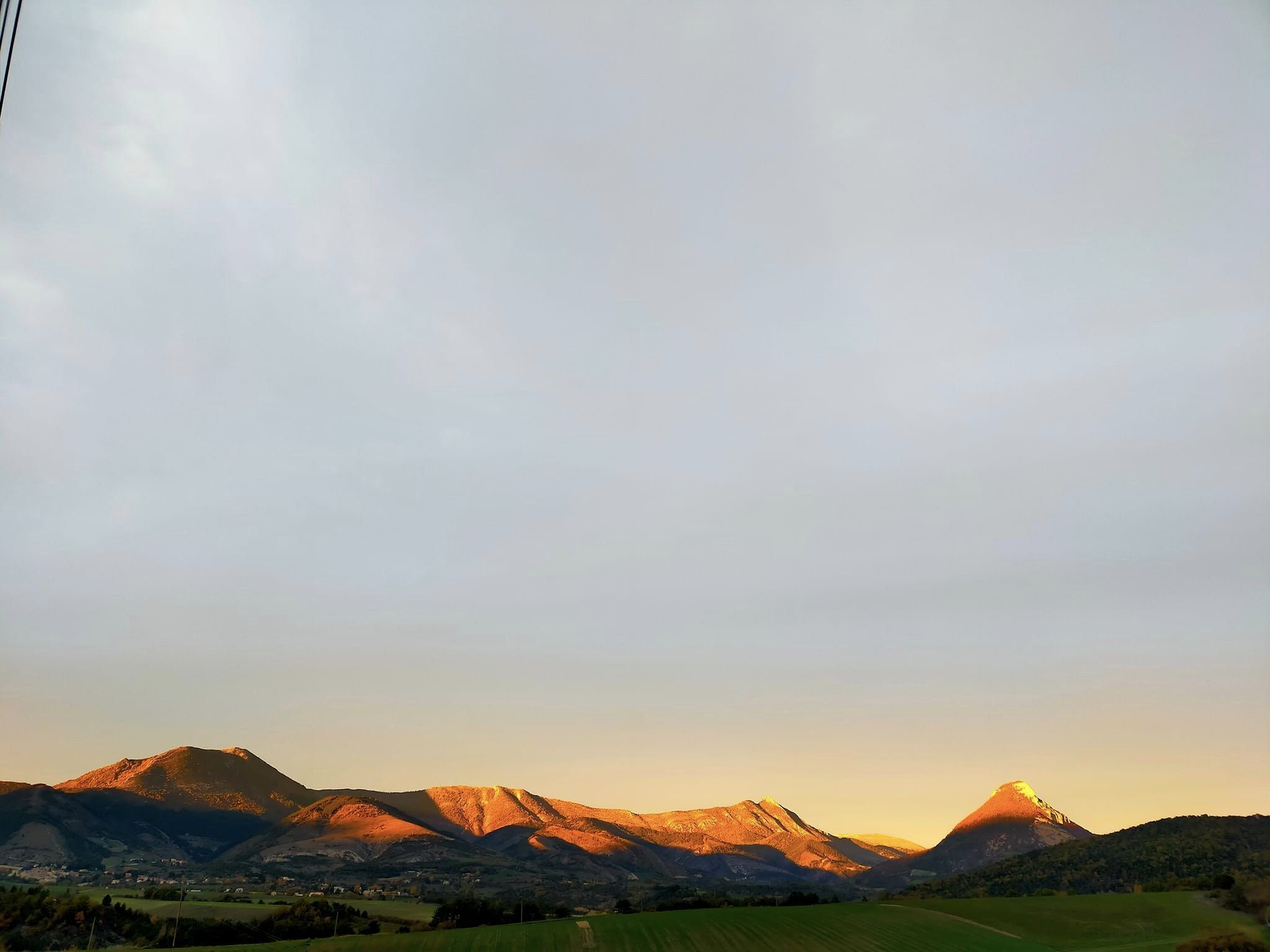 Eine gebirgige Landschaft mit einem Tal und einer kleinen Siedlung im Vordergrund.