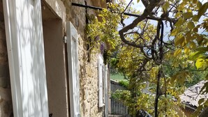 Un étroit sentier en bois, bordé de murs de pierre et d’une clôture métallique, mène à un bâtiment dont les portes sont blanches.