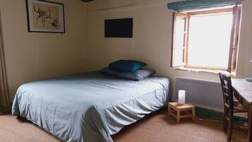 Een kamer met een bed, een klein tafeltje, een stoel, een raam en een ingelijste foto aan de muur.