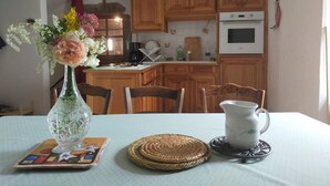 Une table à manger ornée d’un vase de fleurs, d’un pichet en céramique et de sets de table en fibres tressées.