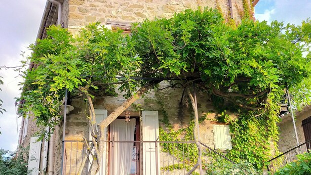 Un bâtiment en pierre avec un toit en tuiles, des murs couverts de lierre et un petit balcon doté d’une rambarde en métal.