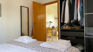 A hotel room with a bed, a wardrobe, a desk with a chair, and a mirror.