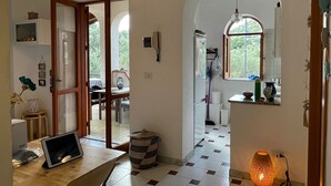 A spacious kitchen with a checkered floor, a wooden dining table, a laptop, a hanging pendant light, and a window with a view of greenery.