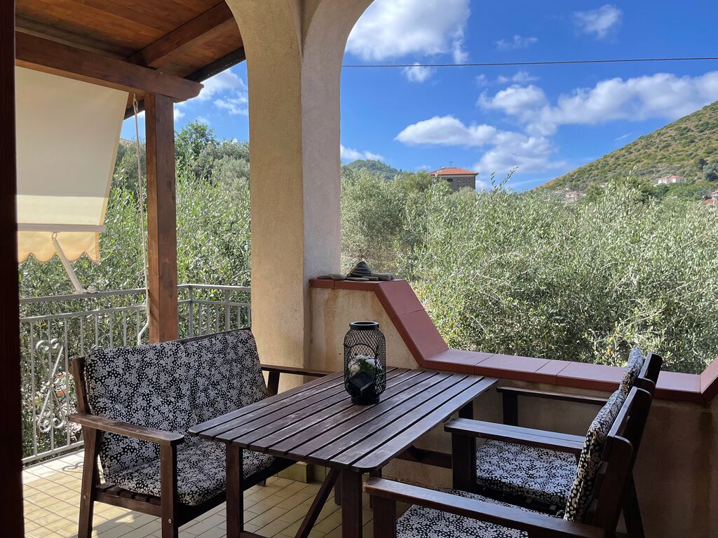 A balcony with a wooden table and two chairs, a lantern, and a view of a hillside with buildings.