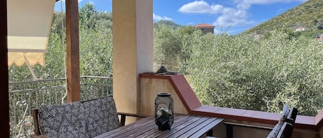 En balkong med ett träbord och två stolar, en lykta och utsikt över en sluttning med byggnader.