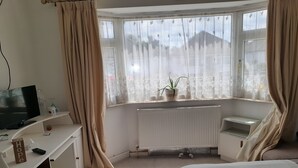 Ein Schlafzimmer mit Bett, Schreibtisch mit Fernseher, Heizkörper und Fenster mit Vorhängen.
