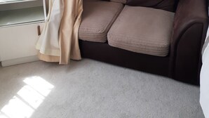 Ein Eckzimmer mit einem braunen Sofa, einem weißen Schreibtisch und einem Fenster mit beigefarbenen Vorhängen.
