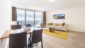 A modern living room with a dining area, large windows, a sofa, and a painting on the wall. - Superior apartment with 1 bedroom & summer pool (Radstadt)