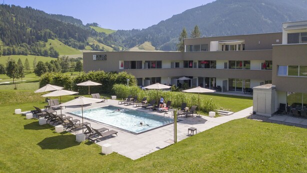 A hotel with a swimming pool, outdoor seating, and a view of mountains. - Superior apartment with 1 bedroom & summer pool (Radstadt)