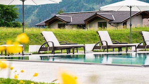 A poolside area with lounge chairs and an umbrella, surrounded by a lush green landscape and a mountain in the background. - Superior apartment with 2 bedrooms & summer pool (Radstadt)