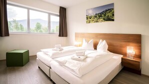 A hotel room with a large bed, a wooden headboard, a bedside table with a lamp, and a view of mountains through the window. - Superior apartment with 2 bedrooms & summer pool (Radstadt)