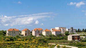 Une rangée d’immeubles résidentiels aux toits orange, entourés de verdure et sous un ciel bleu clair.
