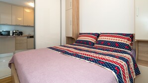 Une chambre avec un lit, une armoire en bois, un coin cuisine et une porte coulissante.