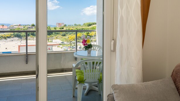 Un balcon avec une table et des chaises en verre, un vase rempli de fleurs et une vue sur la côte.