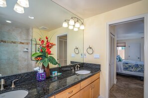 A bathroom with a large mirror, a sink, a vanity, and a shower area.