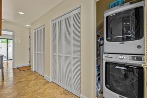 Un cuarto de lavado con lavadora y secadora apiladas, una puerta con paneles y piso de baldosas.