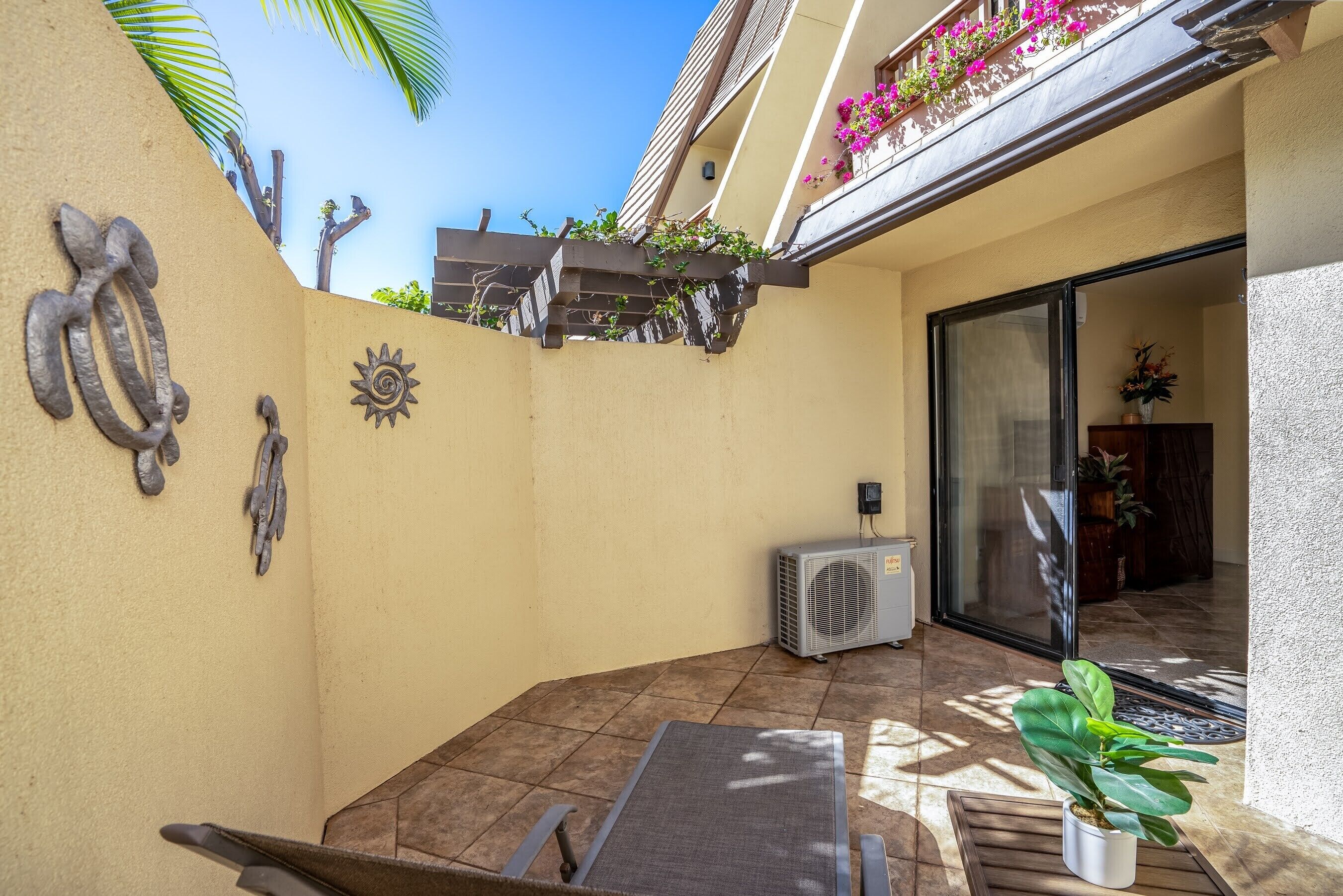 Un patio con una mesa, sillas, una planta en maceta y detalles decorativos en la pared.