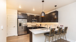 A modern kitchen with dark cabinets, a stainless steel refrigerator, a microwave, and a large island with bar stools.