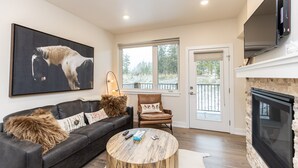 A living room with a fireplace, a large painting of a horse, a leather chair, and a couch with fur throw pillows.