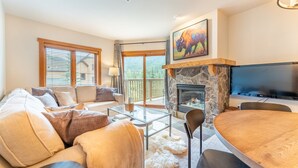 A cozy living room with a stone fireplace, a flat-screen TV, a sofa, and a dining table. - River Run Village Condo is Only a Short Walk to Gondola, Shops and Dining! (Keystone)
