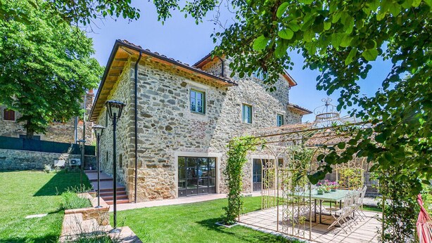 Una casa in pietra con patio sul giardino, una pergola e vista libera sui dintorni.