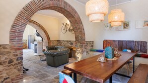 Zona pranzo con tavolo in legno, panche e pavimento in pietra. Si nota un arco in mattoni, una bicicletta e una parete con opere d'arte incorniciate.