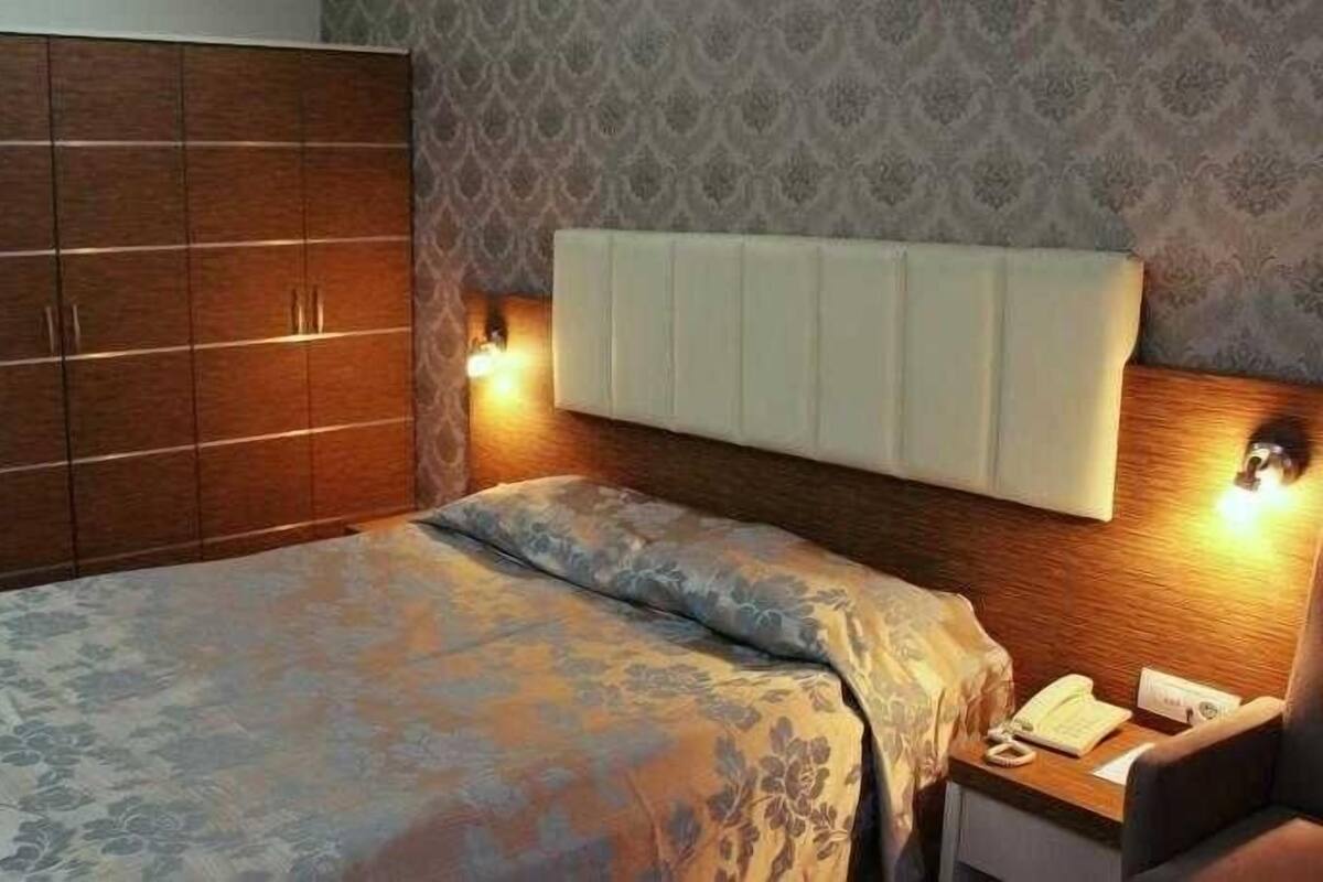 A bedroom with a bed, a wardrobe, a nightstand, and a wall-mounted light fixture.