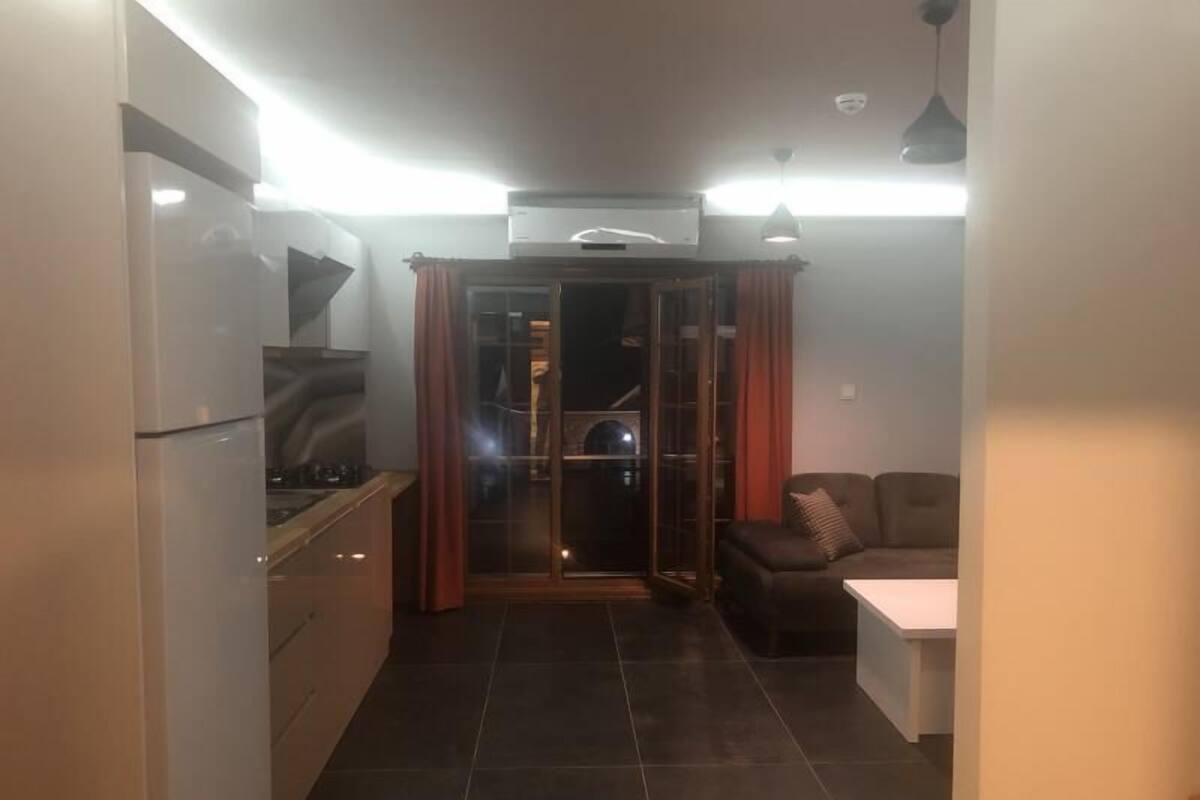 A compact kitchen with a refrigerator, stove, and a sliding glass door leading to a balcony.