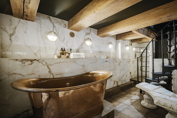 A luxurious bathroom with a large copper bathtub, marble walls, and wooden beams. - Hotel The Noblemen (Amsterdam)