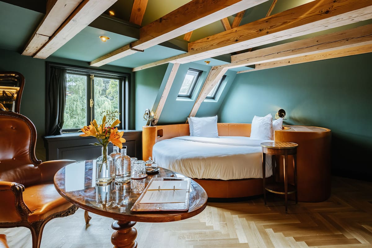 A bedroom with a bed, a wooden table with a vase of flowers, a chair, and a window with curtains.