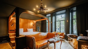 A luxurious bedroom with a four-poster bed, a sitting area with a sofa, a wooden coffee table, and a vintage bathtub. - Hotel The Noblemen (Amsterdam)