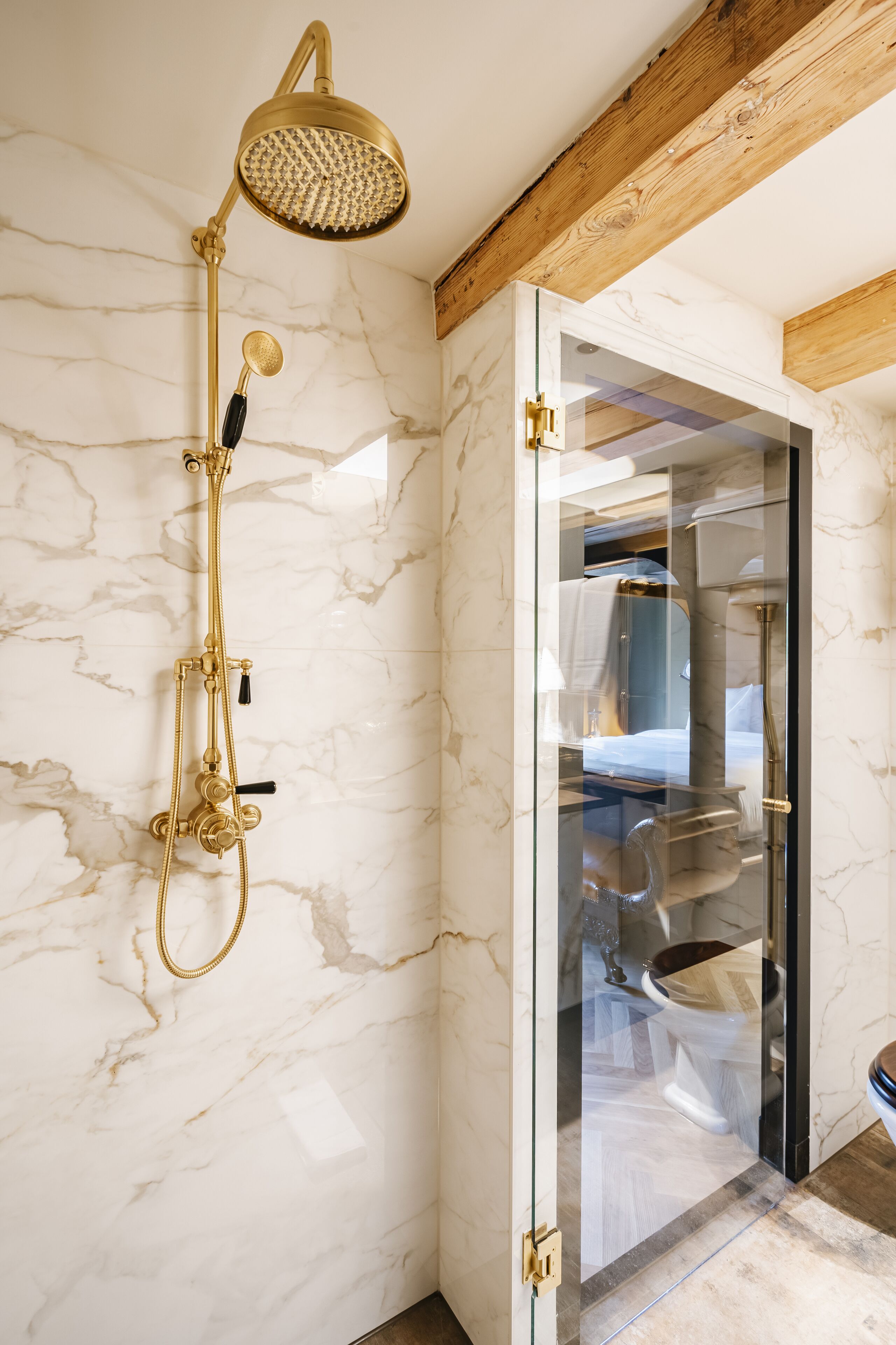 Een badkamer met een gouden douchekop, marmeren wanden en een douchecabine met glazen wanden.