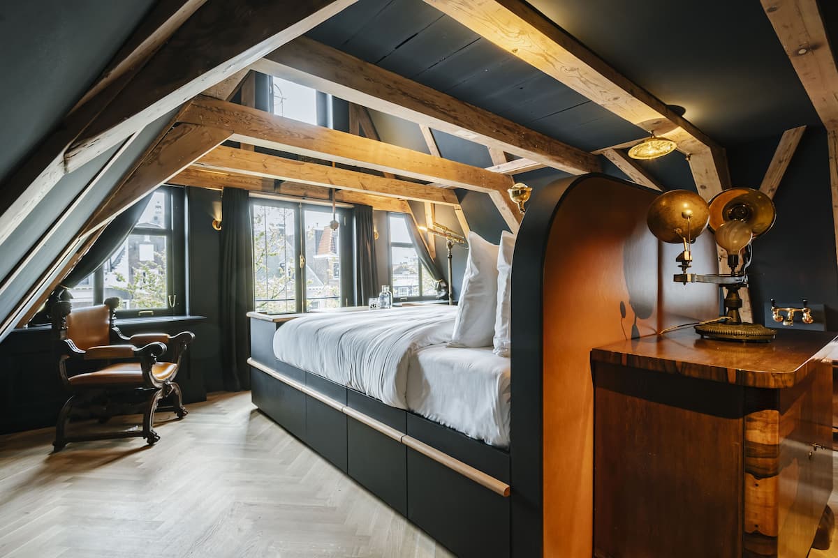 A loft bedroom with a sloped ceiling, built-in wooden bed, and a desk with a lamp.