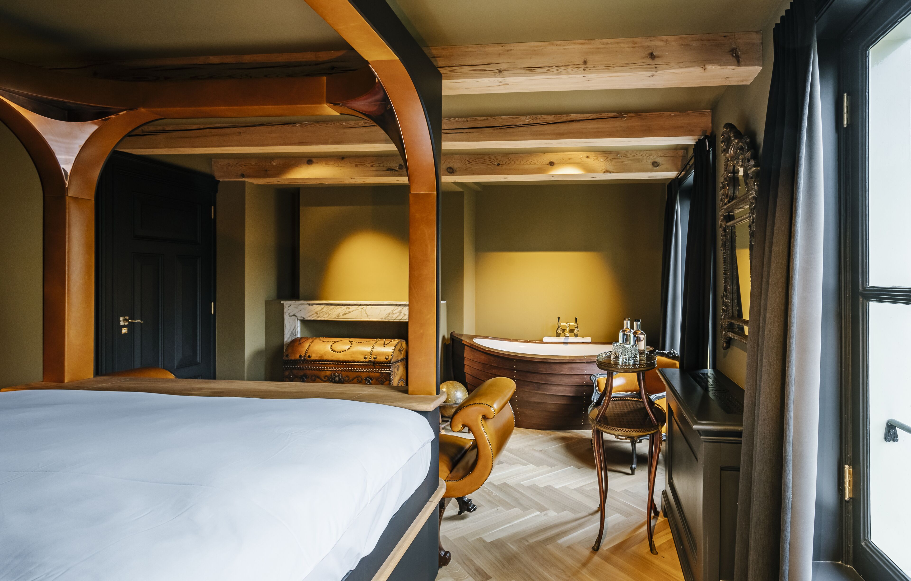 A bedroom with a large bed, a wooden ceiling, a bathroom with a bathtub, and a desk with a chair.