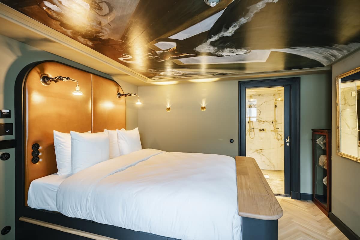 A modern hotel room with a large bed, a wooden headboard, and a ceiling with a unique design.