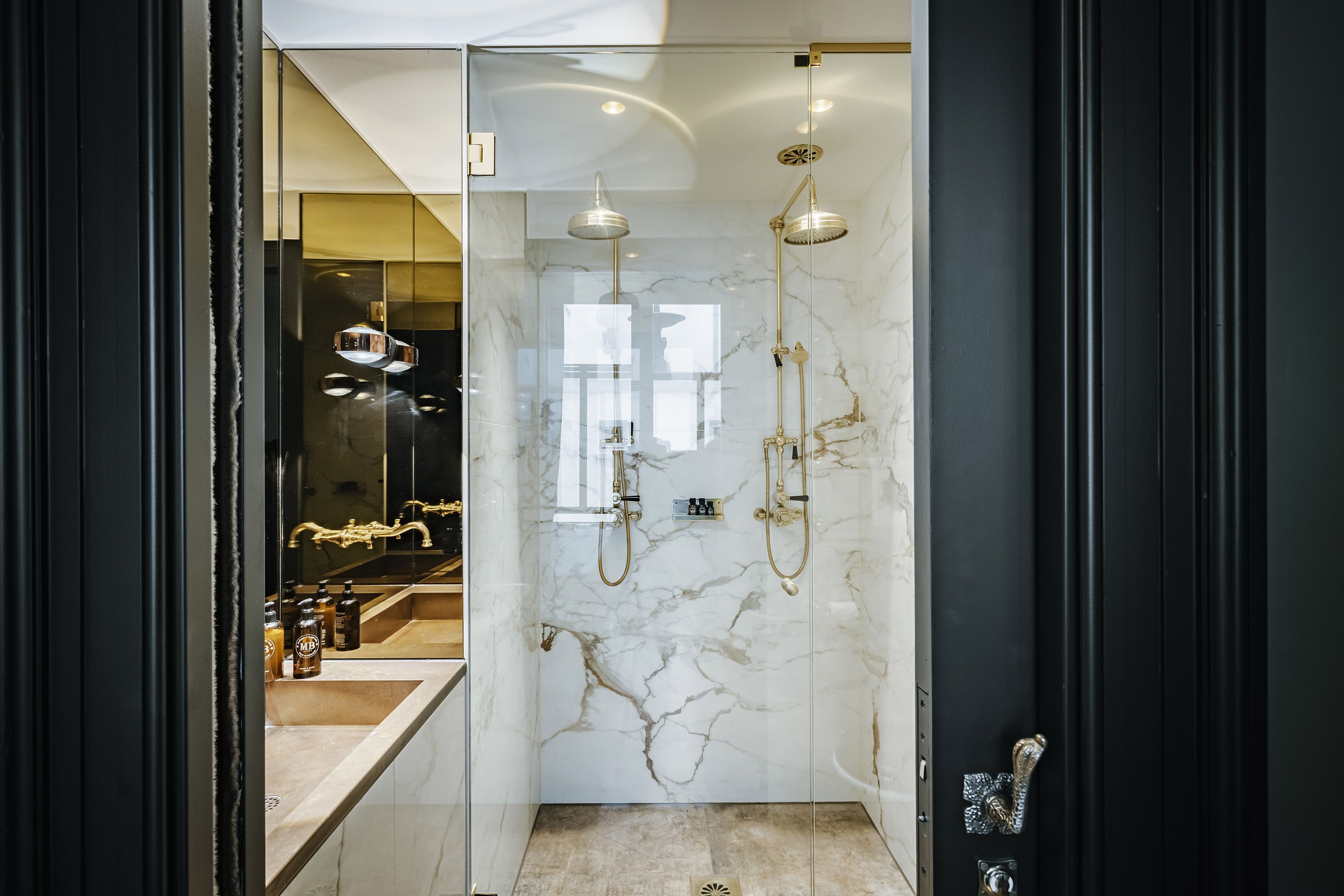 Ein modernes Badezimmer mit einer in Glas abgeschlossenen Dusche, Marmorwänden und einem sichtbaren Waschbeckenbereich.