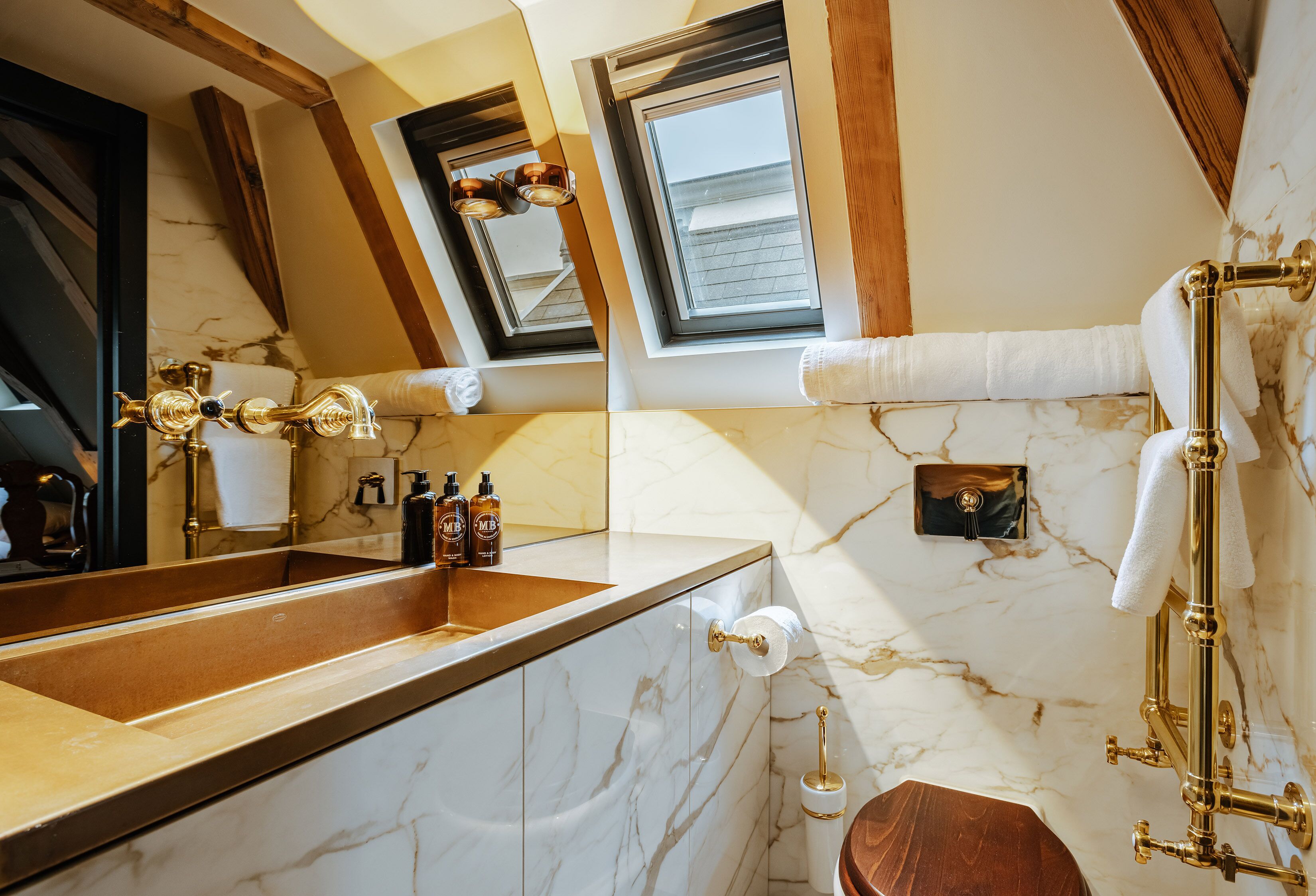 A bathroom with a marble vanity, gold fixtures, and a skylight.