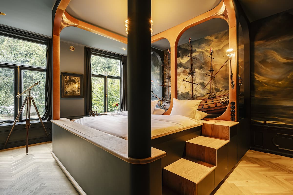 A modern bedroom with a large bed, wooden steps, and a mural of a ship.