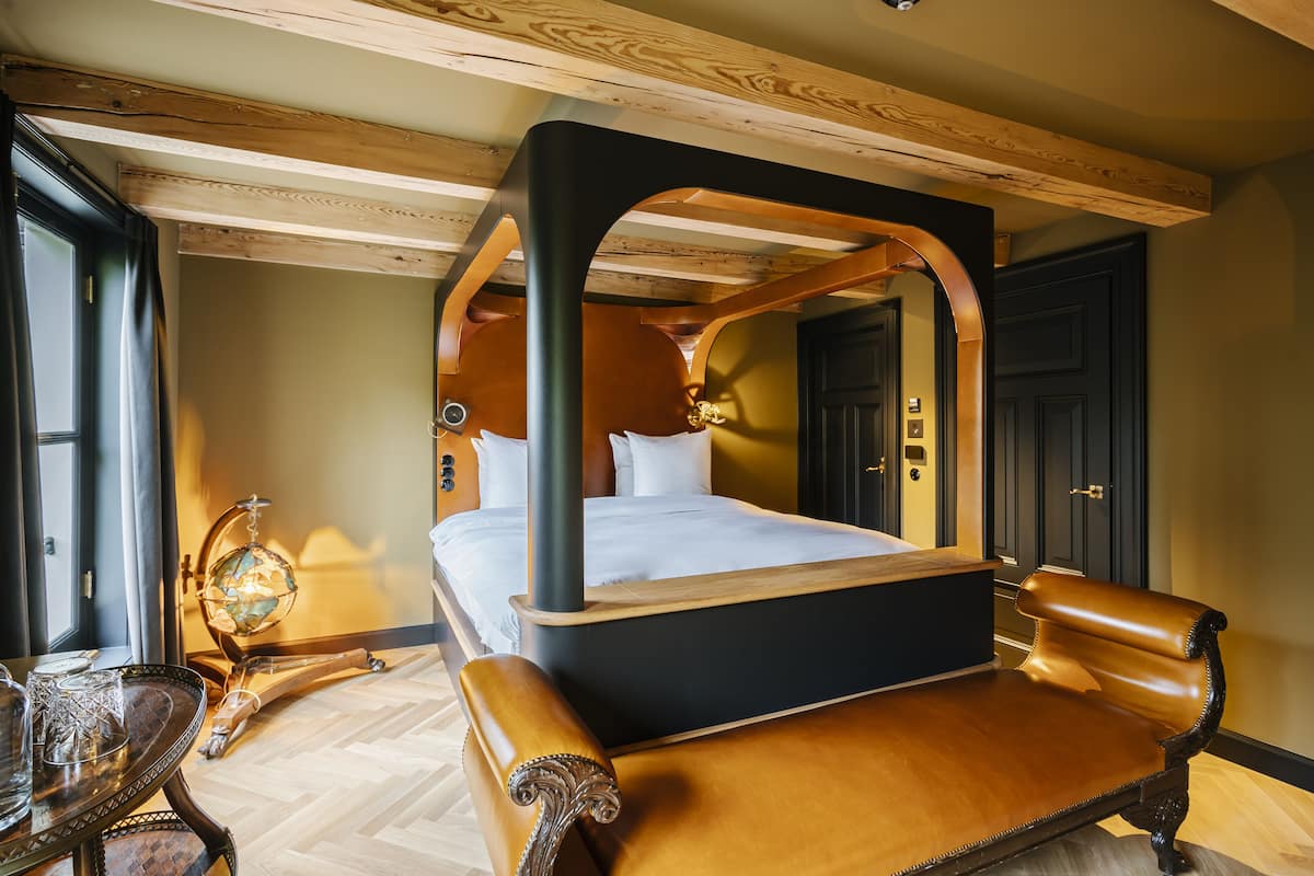 A bedroom with a four-poster bed, wooden ceiling beams, a globe lamp, and a wooden chair.