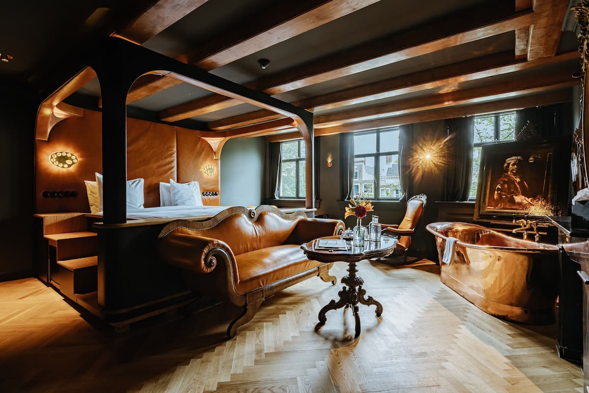 A room with a wooden ceiling, a leather sofa, a round table, and a bathtub.