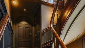 A grand wooden staircase with a curved design, leading to a dark wooden door at the top. - Hotel The Noblemen (Amsterdam)