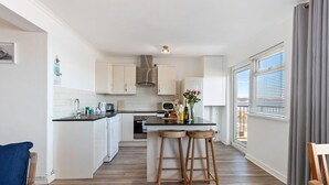 Una cocina moderna con armarios blancos, una encimera negra y taburetes de madera.