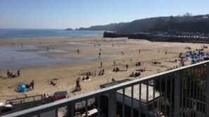 Una playa con gente y sombrillas, cielo despejado y colinas a lo lejos.