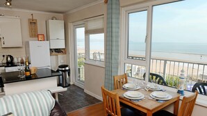 Una cocina con vistas al mar, un comedor con mesa preparada para cuatro personas y una zona de estar acogedora con un cojín a rayas.